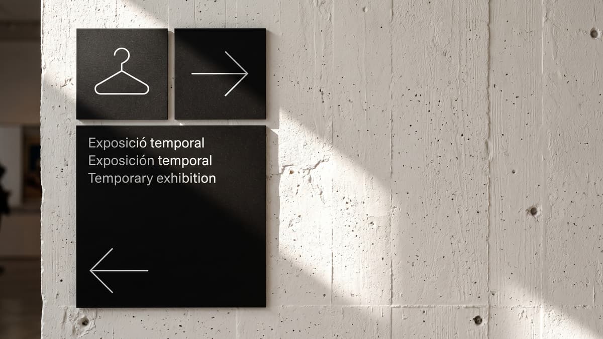 Museum wayfinding concept with thin white arrows and a coat hanger pictogram on black signs